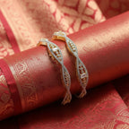 Shangri American Diamond bangles with golden polish and intricate stone detailing on a red silk fabric background.