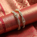 Shangri American Diamond bangles with golden polish and intricate stone detailing on a red silk fabric background.