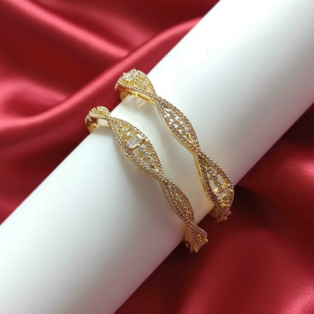 Shangri American Diamond bangles with golden polish and intricate stone-studded twisted design on red satin fabric.