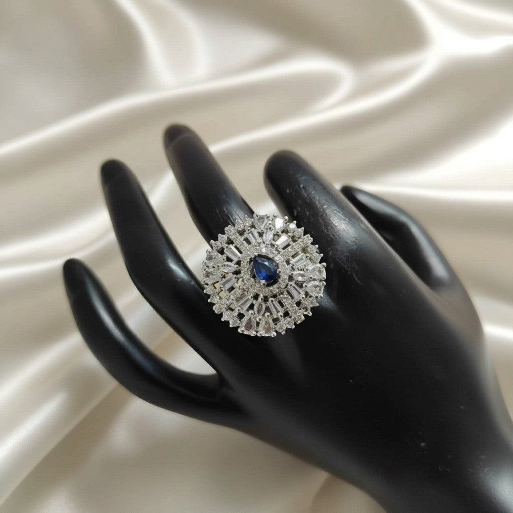Shangri floral halo ring with a blue pear-cut center stone and baguette American diamonds on a black display hand