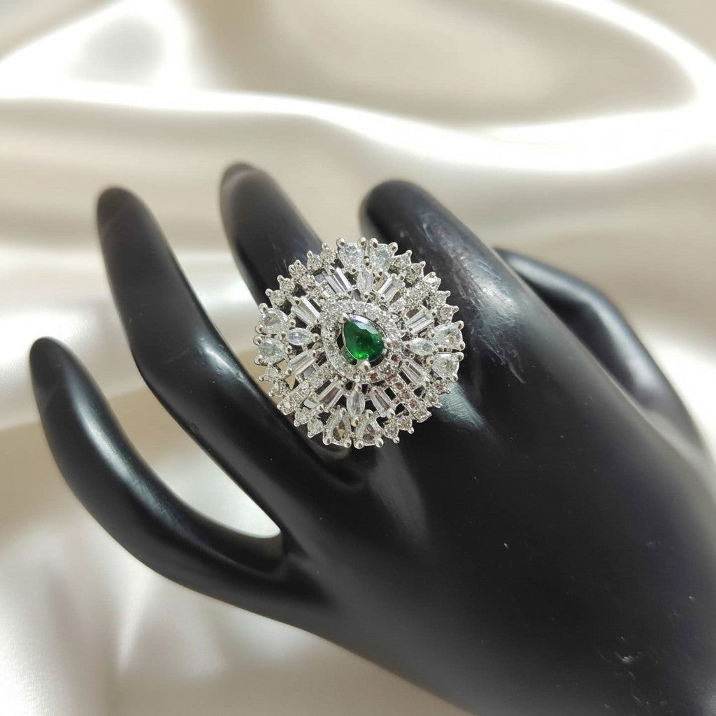 Shangri floral halo ring with a green pear-cut center stone and baguette American diamonds on a black display hand