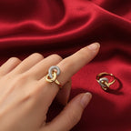 Shangri gold-plated cocktail ring with intertwined loops and sparkling Austrian stones on a red satin background