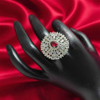 Shangri American Diamond floral halo ring with a red pear-cut center stone on a black display hand against red silk.